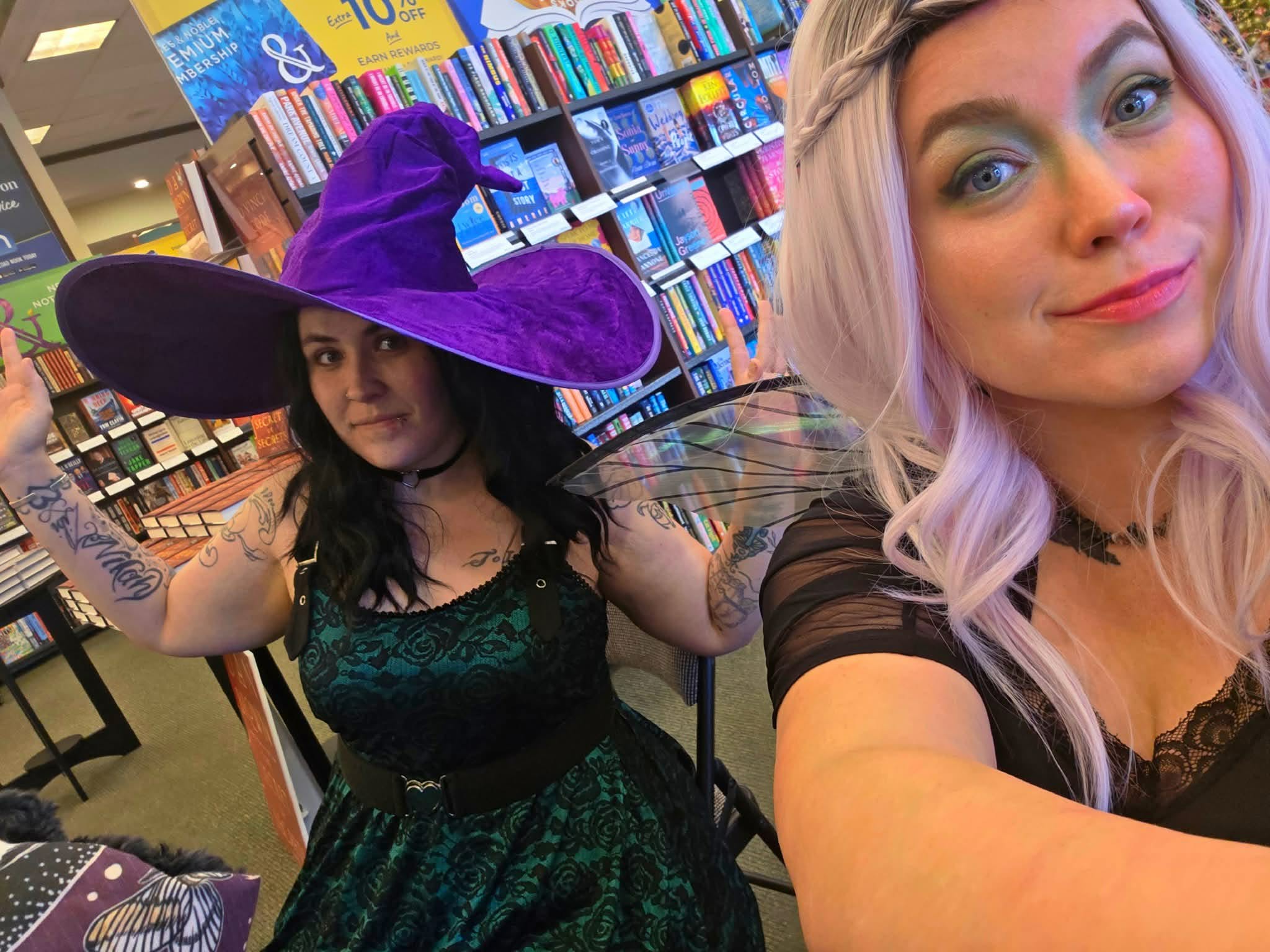 Aj Castelletto as Muse in a purple witch hat beside a friend dressed as Lark in a bookstore